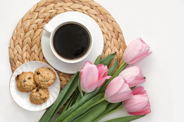 White cup of coffee with pink tulips on white background. Morning coffee on wicker tray. View from above of morning coffee, cookies and flowers. Flat lay. Breakfast in bed. Stylish home interior decor