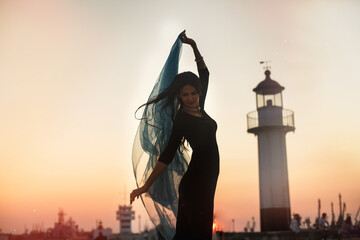 A young woman on the background of a lighthouse during sunset on the seashore. Beautiful slender...