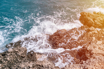 foamy waves of clear blue sea water beat against the rocky shore of the ocean. flare