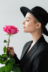 side view of trendy woman with natural makeup holing pink rose isolated on grey.