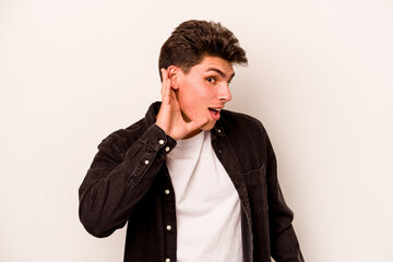 Young caucasian man isolated on white background trying to listening a gossip.