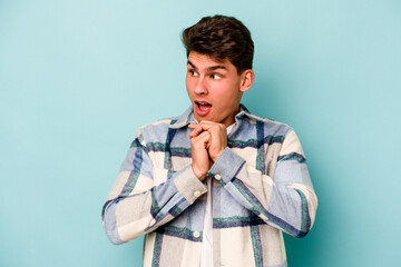Young caucasian man isolated on blue background praying for luck, amazed and opening mouth looking to front.