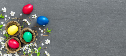 Chicken nests with painted Easter eggs on dark tabletop. Concept creative banner. Holiday greeting card.