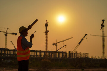 silhouette of Engineer and Worker working at Industrial Building Real Estate project site.Team of Specialists Inspect Commercial, Project with large building. In the Background Crane Skyscraper.