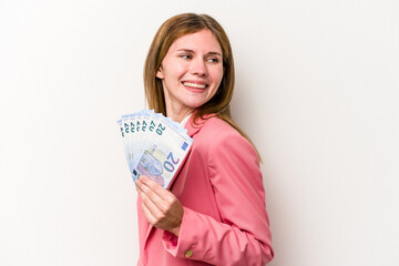 Young business English woman holding banknotes isolated on white background looks aside smiling, cheerful and pleasant.