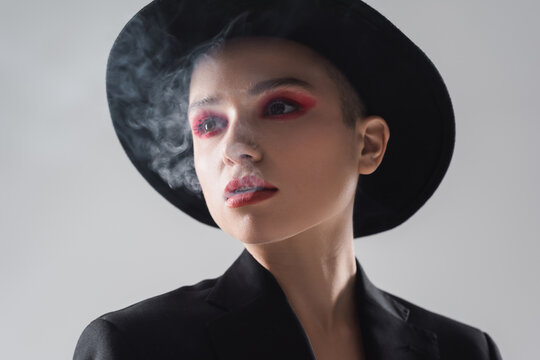 Portrait Of Woman With Carmine Red Makeup Exhaling Smoke Isolated On Grey.