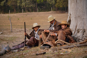 Vintage action shot of a group of cowboys relaxing under a tree. with soft sunlight in the morning