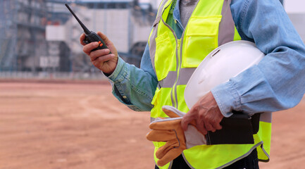 An electrical engineer or middle-aged worker holding a radio transmitter and a hard hat in his hand.