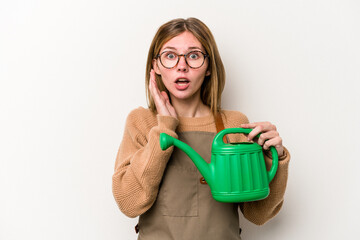 Young gardener woman holding a sprinkler isolated on white background surprised and shocked.