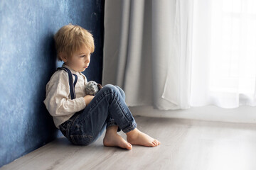 Cute blond preschool boy, sitting on the floor with pet dog, punished for mischief
