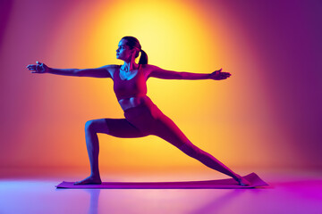 Fototapeta na wymiar Portrait of young sportive girl doing yoga exercises isolated over gradient pink and yellow background in neon.