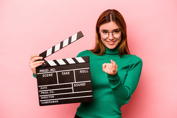 Young caucasian woman holding a clapperboard isolated on pink background pointing with finger at...