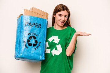 Young woman holding a recycling bag full of paper to recycle isolated on white background showing a copy space on a palm and holding another hand on waist.