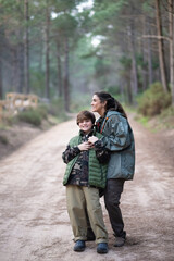 Happy mother and son walking in forest together. Dark-haired woman and boy in coats walking on cloudy day. Family, nature, leisure concept