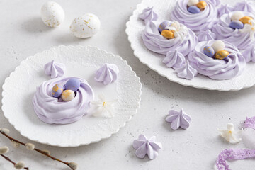 Obraz na płótnie Canvas Easter dessert Mini Pavlova Birds Nests with colorful eggs candy on a light background. Lilac Meringue Cookies. Festive Food recipe. Confectionery, bakery concept. Easter greeting card.
