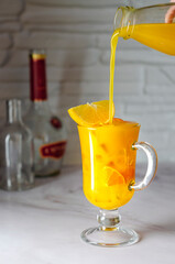 Freshly squeezed orange and sea buckthorn juice with orange ice is poured from a bottle on a table, decorated with an orange slice