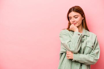 Young caucasian woman isolated on pink background looking sideways with doubtful and skeptical expression.
