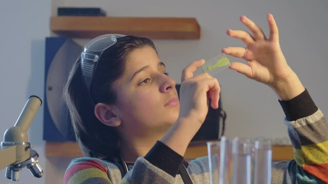 A young scientist examines a leaf of a plant on a glass slide through a microscope. School science project in biology