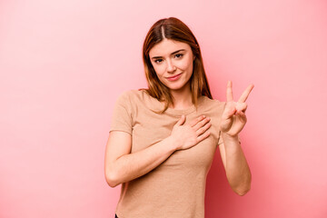 Young caucasian woman isolated on pink background taking an oath, putting hand on chest.