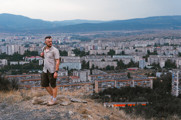 A tourist man with backpack poses against the backdrop of a densely populated area. Top view. skyscrapers. Tbilisi Georgia. Zghvisubani III Micro-District. Copy space. Travel and vacation