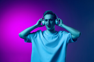 Portrait of young emotive man listening to music in headphones isolated over gradient pink and...