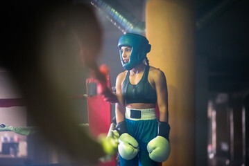 Portrait of young girl ready to go out on ring. Sporty girl in protective helmet and gloves preparing for sparring, standing near ring looking at her rival. Sport activity, healthy lifestyle concept - Powered by Adobe