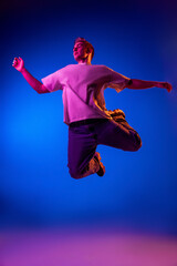 Portrait of young man in casual cloth jumping, posing isolated over blue background in pink neon...