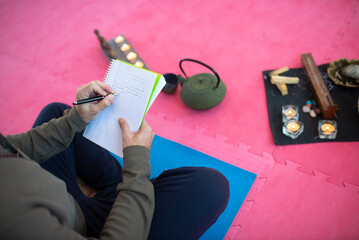 Top view of man writing in notebook in meditation room. Man in casual clothes sitting in lotus...