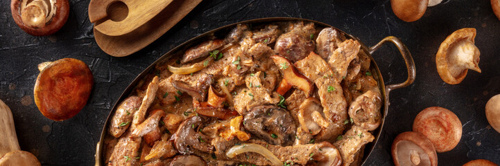 Mushroom beef stroganoff panorama. Meat with champignons, boletus and ceps, overhead flat lay shot on a black background
