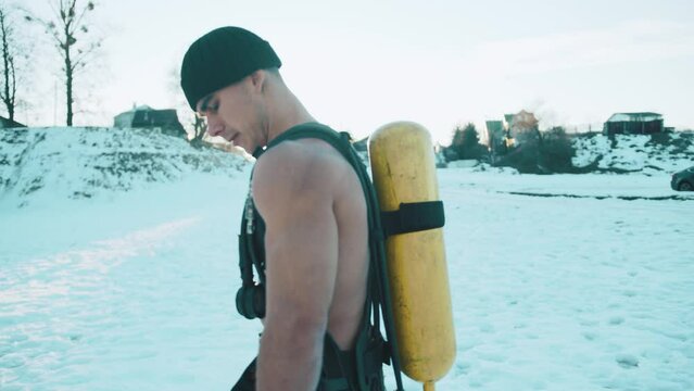 Bodybuilder with a naked torso stands against the backdrop of the sun in a winter park with a ballon compressed air drager on his back