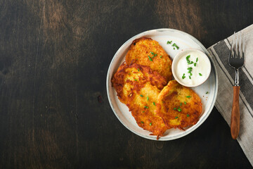 Potato pancakes. Fried homemade potato pancakes or latkes with cream and green onions in rustic plate on old wooden black table background. Rustic style. Healthy food. Top view.