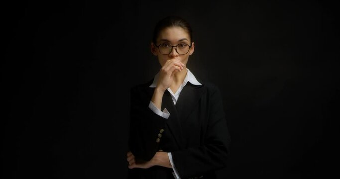 Serious businesswoman in glasses and office black and white clothes smokes an electronic cigarette. Asian woman vaping on isolated black background