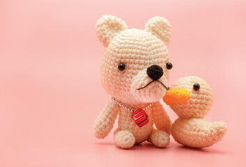 Cute handmade knitted teddy bear and duck dolls isolated on pastel pink background with copy space