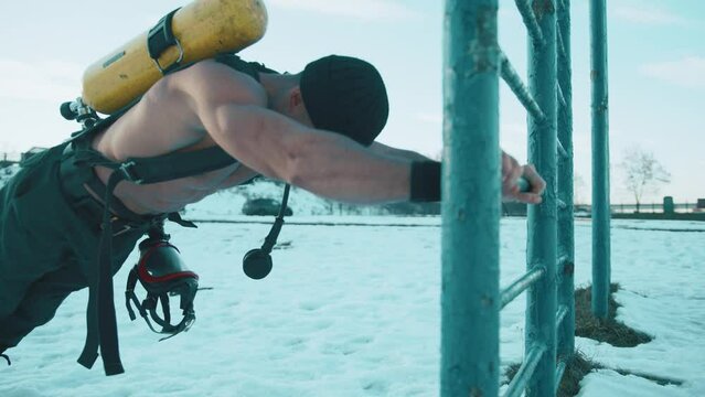 Muscular shirtless man training in winter park and doing strength exercises with drager compressed air balloon on his back