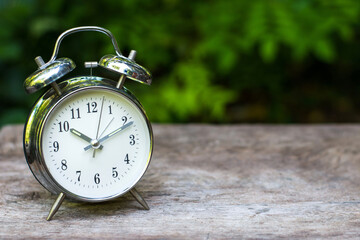 Silver vintage alarm clock on wooden table with nature blurred background