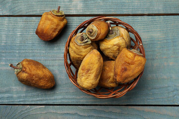 Wicker basket with tasty dried persimmon fruits on light blue wooden table, flat lay