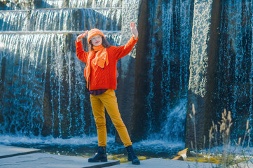 inspirational autumn portrait of a girl in an orange hat and sweater on the background of a waterfall.