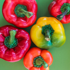 yellow, orange and red peppers on a green background, top view, texture of colorful vegetables, square format  