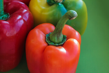 close up of orange pepper on a green background and red and yellow peppers in the background 