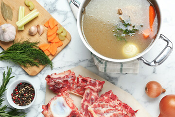 Delicious homemade bone broth and ingredients on white marble table, flat lay