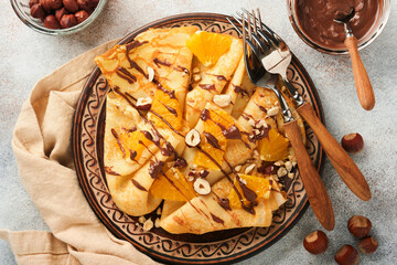 Crepes suzette with oranges and chocolate. Thin crepes with chocolate spread, hazelnuts and orange slices fruit in plate for breakfast on old concrete rustic table background. Copy space. Top view