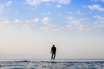 man wearing a long jacket walking on the water during a sunrise, Wet businessman walking to the water