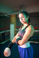 Portrait of sporty boxer girl posing for camera. Pretty young girl in sportswear and gloves standing on ring in gym and proudly looking at camera. Female boxing, hobby and healthy lifestyle concept