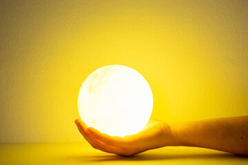 Moon lamp turn on with yellow background hold by one hand