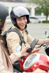 Fototapeta premium Portrait of smiling young man in protective helmet sitting on scooter and talking to friend