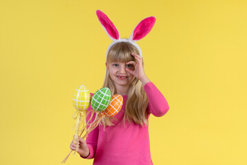Blonde little girl with Easter eggs on a yellow background