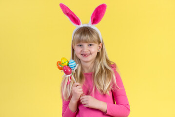 Blonde little girl with Easter eggs on a yellow background