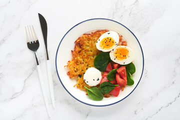 Breakfast. Potatoes latkes with sour cream, spinach salad, tomatoes and boiled eggs on light marble table background. Delicious food for breakfast. Top view.