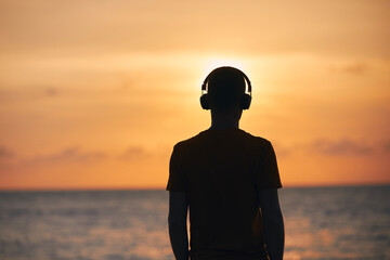 Silhouette of man with headphones against ocean. Serenity, contemplation and listening music at...