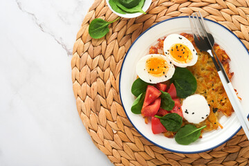 Breakfast. Potatoes latkes with sour cream, spinach salad, tomatoes and boiled eggs on light marble table background. Delicious food for breakfast. Top view.